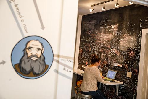 Student sitting at counter in Literary House kitchenette in front of chalkboard wall with phrases and words written in chalk